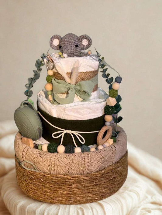 Neutral safari elephant diaper cake baby shower centerpiece featuring three tiers of rolled white diapers wrapped in burlap, soft sage ribbon, and a black accent band with twine bow detail. Top tier decorated with a crocheted gray elephant plush and dried bunny tail grass for a rustic boho touch.

Adorned with eucalyptus greenery garland and silicone and crochet beaded pacifier clips in forest green, beige, and natural wood tones. Includes a matching sage green pacifier case attached to the side and natural