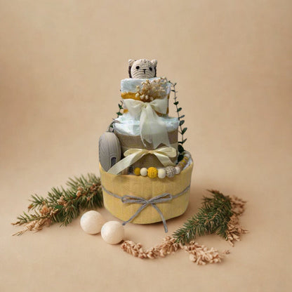 Sunny woodland diaper cake baby shower centerpiece featuring three tiers of rolled white diapers in soft yellow, cream, and natural tones. The base tier is wrapped in warm pastel yellow fabric and finished with a delicate gray twine bow for a subtle rustic touch.

The middle tier is accented with natural burlap ribbon and a soft ivory satin bow, complemented by a coordinating silicone and crochet beaded pacifier clip in shades of mustard, cream, and light gray. A matching neutral pacifier case is tucked nea