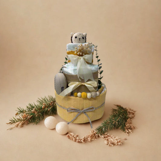 Sunny woodland diaper cake baby shower centerpiece featuring three tiers of rolled white diapers in soft yellow, cream, and natural tones. The base tier is wrapped in warm pastel yellow fabric and finished with a delicate gray twine bow for a subtle rustic touch.

The middle tier is accented with natural burlap ribbon and a soft ivory satin bow, complemented by a coordinating silicone and crochet beaded pacifier clip in shades of mustard, cream, and light gray. A matching neutral pacifier case is tucked nea