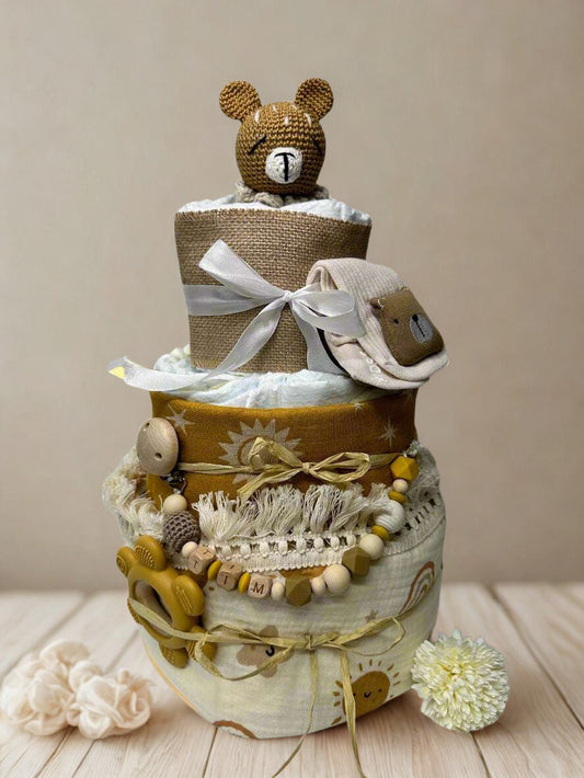 Sunshine teddy bear diaper cake baby shower centerpiece featuring three tiers of rolled white diapers styled in warm mustard, cream, and natural burlap tones. The base tier is wrapped in soft cream fabric with subtle rainbow and sunshine prints, tied with rustic raffia for a charming boho finish.

The middle tier showcases rich mustard fabric adorned with delicate sun and star motifs, accented with fringe trim and natural twine for added texture. A coordinating silicone and wooden beaded pacifier clip in sh