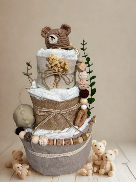Neutral teddy bear diaper cake baby shower centerpiece featuring three tiers of rolled white diapers in soft beige, taupe, and natural linen textures. The base tier is wrapped in warm gray fabric and finished with a rustic rope accent for a cozy, modern touch.

The middle tier is adorned with burlap-style fabric and tied with delicate twine, complemented by a silicone and crochet beaded pacifier clip in earthy tones of cream, mocha, blush, and walnut. Wooden letter beads spelling “BABY” add a charming perso