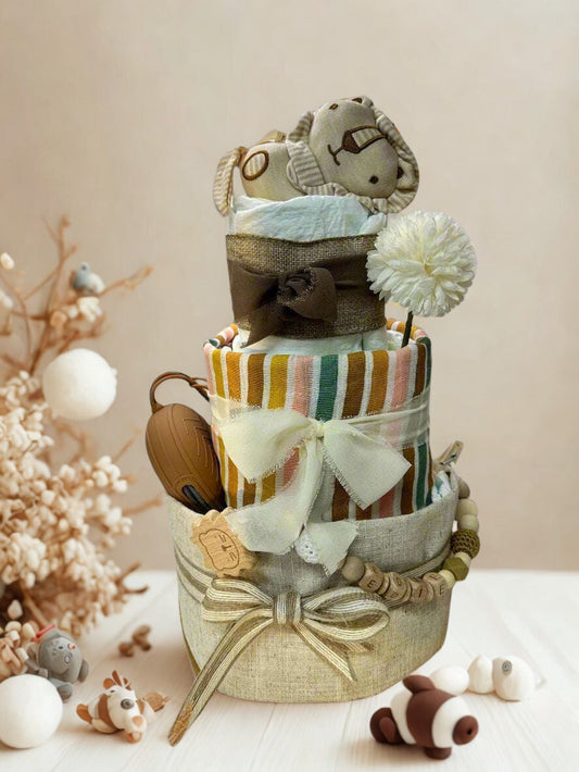 Three-tier neutral safari diaper cake featuring rolled white diapers wrapped in natural linen and multicolor earth-tone striped fabric in shades of mustard, rust, sage, and cream. The base tier is finished with a soft sage bow, while the middle tier showcases a coordinating striped design tied with an ivory ribbon.

The top tier is wrapped in rustic burlap and crowned with a soft plush elephant toy resting on top. A white decorative flower adds an elegant accent. The cake includes a brown silicone pacifier 