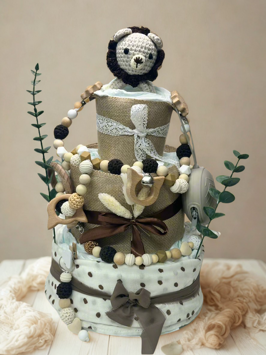 Three-tier neutral safari diaper cake featuring rolled white diapers wrapped in burlap and soft polka dot fabric in cream and taupe tones. The base tier is tied with a mocha ribbon bow, while the middle tier is accented with a rich brown satin ribbon and dried floral details for a rustic touch.

The top tier is finished with delicate lace trim and crowned with a handmade crocheted lion plush in soft cream with a dark brown mane. The cake is decorated with coordinating wooden and silicone beaded pacifier cli