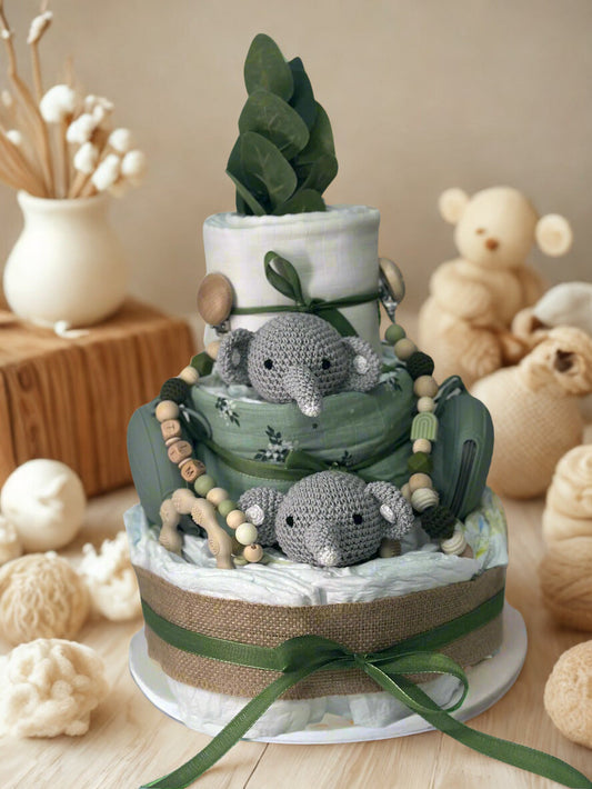 Green safari elephant diaper cake baby shower centerpiece featuring three tiers of rolled white diapers styled in rich sage and earthy neutral tones. The base tier is wrapped in burlap and finished with a deep olive satin ribbon bow, creating a warm woodland foundation.

The middle tier showcases soft green botanical fabric and is adorned with a coordinating silicone and crochet beaded pacifier clip in shades of moss, cream, and natural wood. Matching green pacifier cases are placed on both sides for a bala