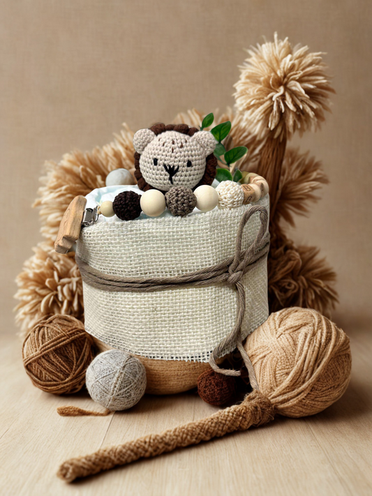 Rustic lion diaper cake baby shower centerpiece designed in warm neutral tones and natural textures. This single-tier diaper arrangement is wrapped in soft ivory burlap-style fabric and finished with a taupe cotton rope bow for a cozy, handcrafted look.

Topped with an adorable handmade crocheted lion plush featuring a soft beige face and chocolate brown mane, this charming safari detail adds a sweet woodland touch. A coordinating silicone and crochet beaded pacifier clip in shades of cream, mocha, and dark