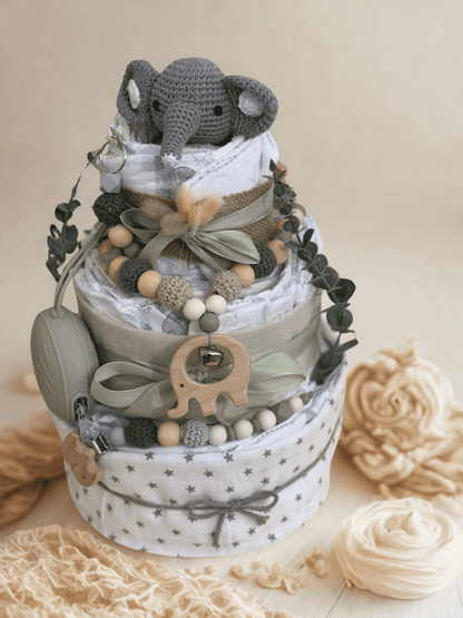 Neutral elephant diaper cake baby shower centerpiece featuring three tiers of rolled white diapers wrapped in soft gray fabric with delicate star print and natural burlap ribbon. Top tier decorated with a crocheted gray elephant plush, accented with dried bunny tail grass and a sage green satin bow for an elegant boho touch.

Embellished with eucalyptus greenery, silicone and crochet beaded pacifier clips in muted green, beige, and gray tones, and natural wooden bead garlands. Includes a wooden elephant-sha
